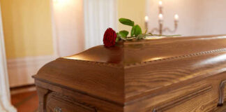 A wooden casket with a red rose on top, set in a softly lit room