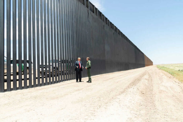 Two people standing near tall border wall outside