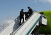Police officers escorting a passenger down the stairs from an airplane