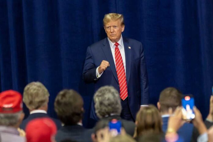 A man in a suit with a red tie standing confidently in front of an audience