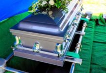 A silver casket adorned with flowers at a graveside