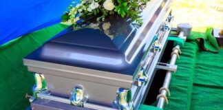 A silver casket adorned with flowers at a graveside