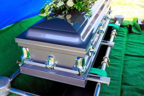 A silver casket adorned with flowers at a graveside