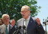 Man speaking at outdoor press conference with microphones