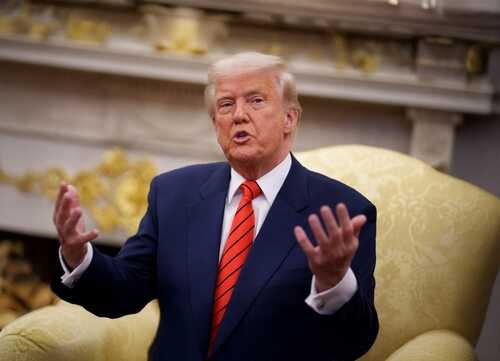 A man in a suit speaking with expressive hand gestures in a formal setting