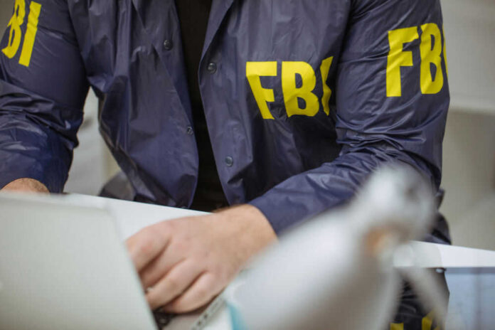 Person wearing FBI jacket using a laptop