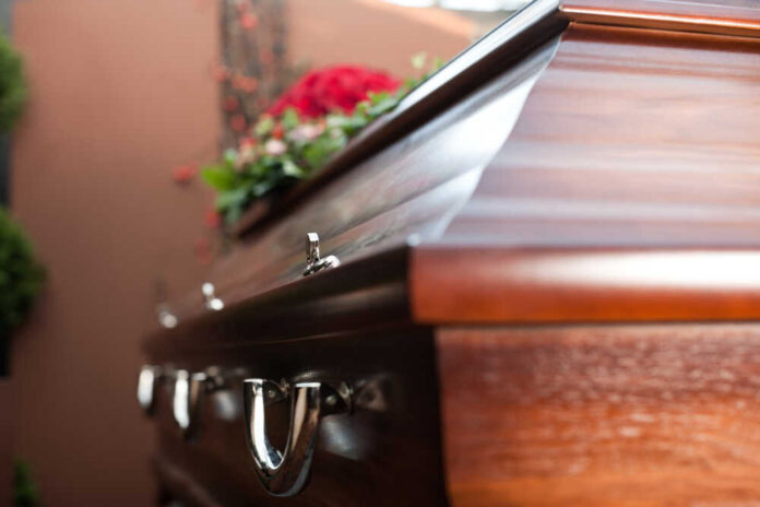 Close-up of a wooden casket adorned with flowers in a funeral setting
