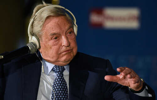 An older man in a suit speaking at a conference with a microphone and headphones