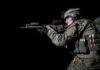Soldier aiming rifle in tactical gear against black background