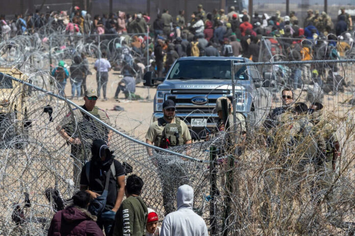 Crowded border fence with people and law enforcement officers