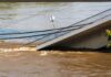 A partially collapsed bridge over a brown river due to flooding