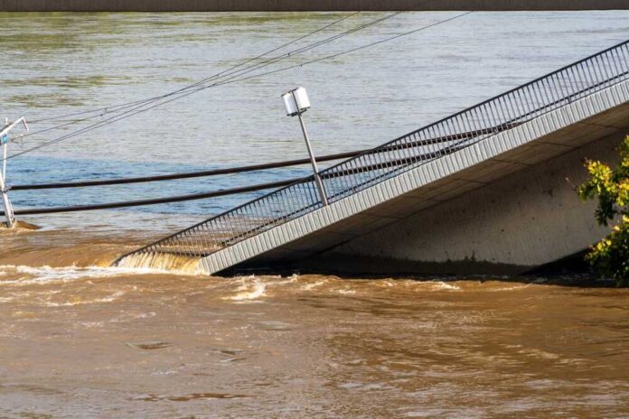A partially collapsed bridge over a brown river due to flooding
