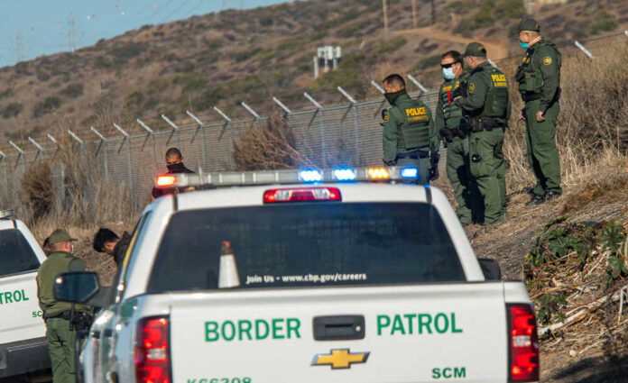 Border Patrol agents gathered near a fence outdoors