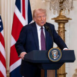 Man speaking at podium with USA and UK flags