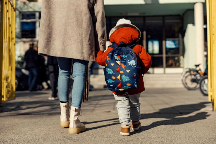 Child with dinosaur backpack walking beside adult