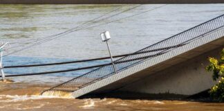 A partially collapsed bridge over a brown river due to flooding