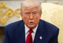 Man in suit with red tie speaking indoors