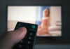 Hand holding remote facing blurred television screen